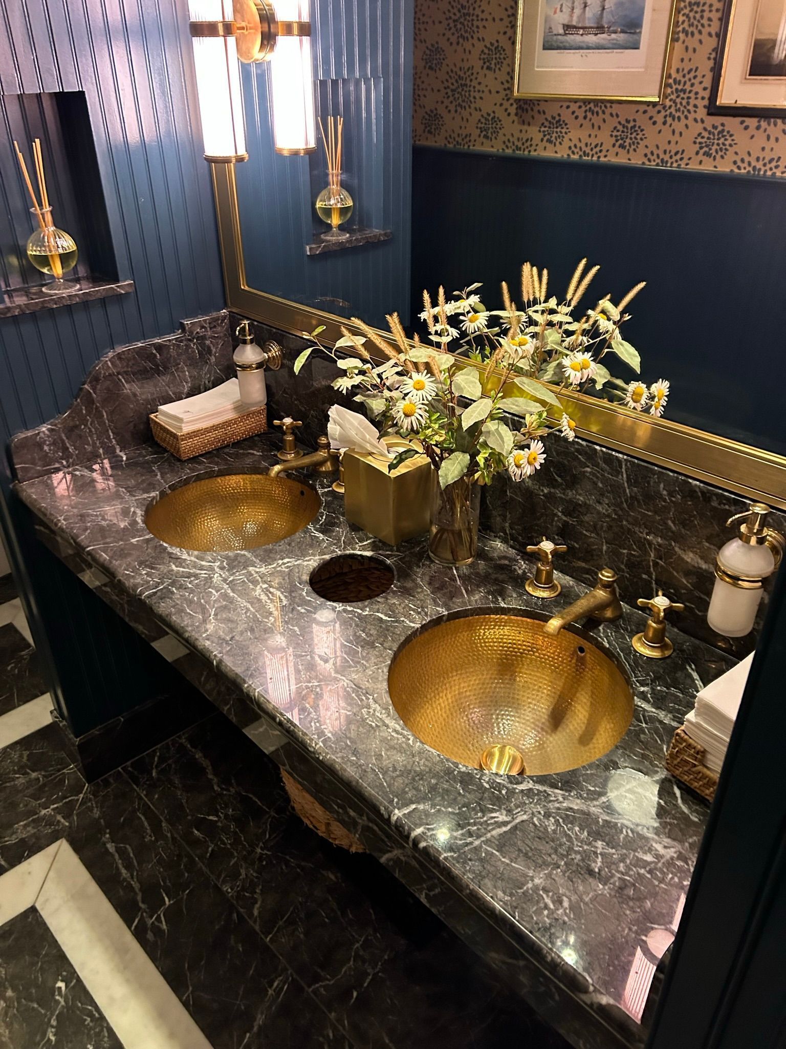 Luxurious bathroom with gold sinks, dark marble countertop, and floral arrangement.