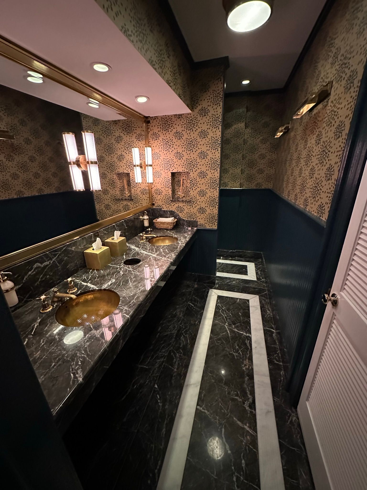 Luxury bathroom with black marble countertop and floor, gold accents, patterned wallpaper, and recessed lighting.