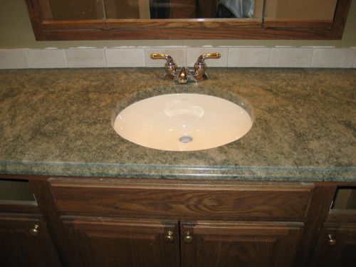 Bathroom vanity with oval sink, brown countertop, wooden cabinet, and gold-toned faucet.