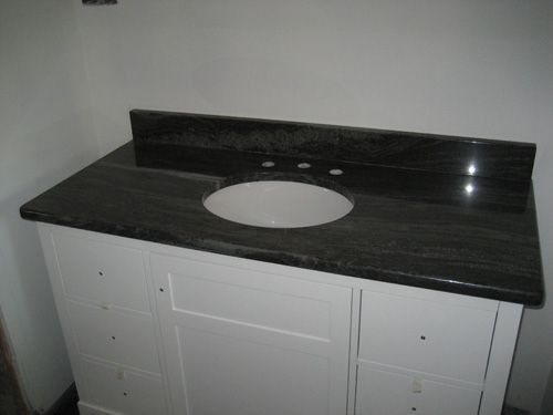 White bathroom vanity with dark granite countertop and a round sink basin.