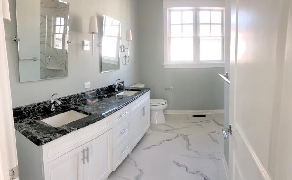 Bathroom with double vanity, marble countertops, white cabinets, and large window.
