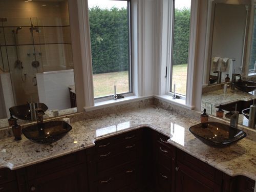 Bathroom with brown cabinets, granite countertop, two glass vessel sinks, and a window overlooking a yard.