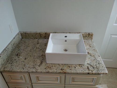 Bathroom vanity with white square sink on a granite countertop, above cream-colored cabinets, against a white wall.