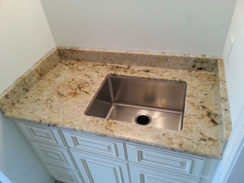 Stainless steel sink in a light granite countertop over a white cabinet.