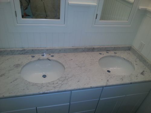Double sink bathroom vanity with marble countertop, oval sinks, and white cabinets.