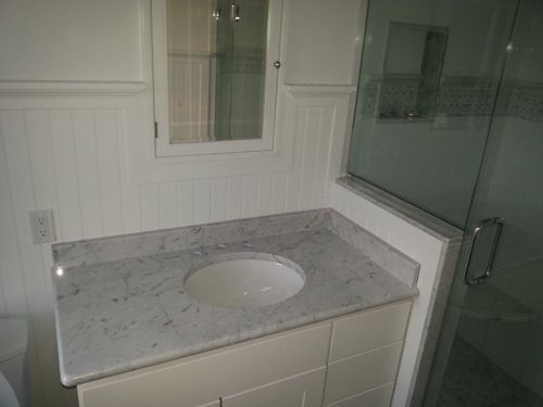 Bathroom with a white vanity, marble countertop, and glass shower door.