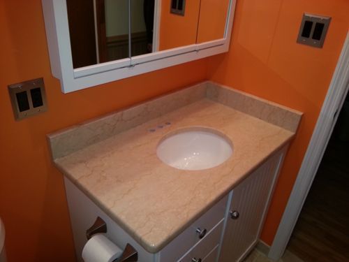 Bathroom with orange walls, a white vanity with a tan countertop, and a round sink.