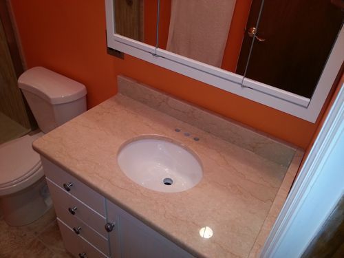 Bathroom with white vanity, tan countertop and oval sink, orange wall, toilet, and mirror.