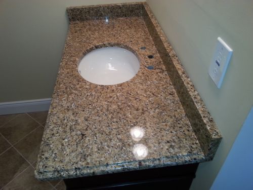 Granite bathroom vanity with a white, round sink; beige walls, brown tile floor.
