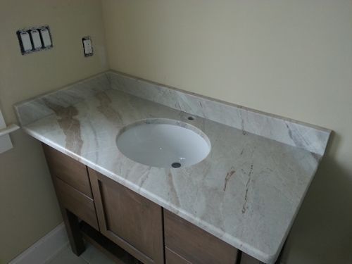 Bathroom vanity with a light-colored countertop, oval sink, and wooden cabinet, against a beige wall.