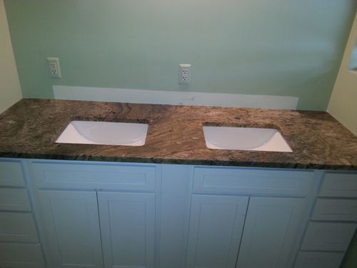 Bathroom vanity with two sinks, granite countertop, white cabinets, and light green wall.