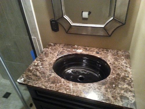 Bathroom vanity with brown marbled countertop, black sink, and beveled mirror.