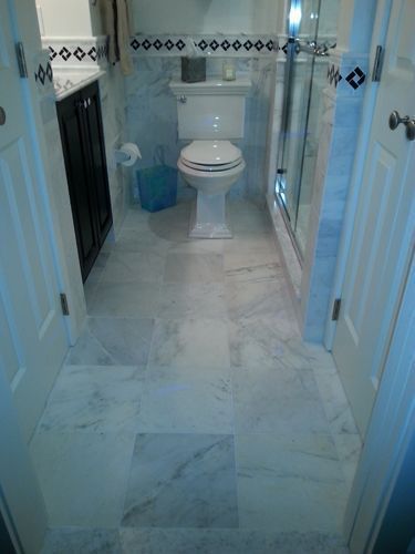 Bathroom with marble floor, toilet, shower, and dark cabinet. Blue and white accents on walls.