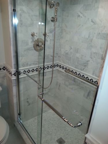 Glass-enclosed shower with silver fixtures, marble tile walls, and a decorative border.