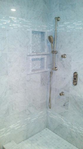 Marble-tiled shower with built-in shelves and silver shower fixtures.