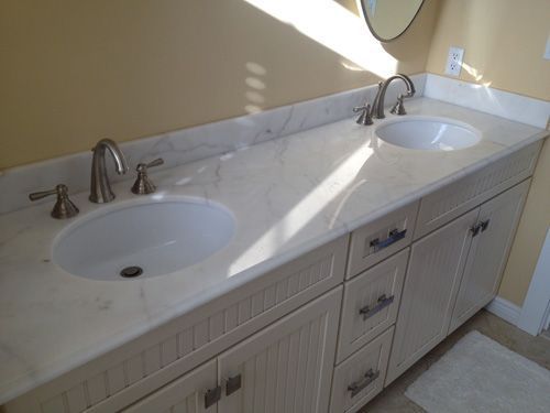 White bathroom vanity with two sinks, marble countertop, and brushed nickel faucets.