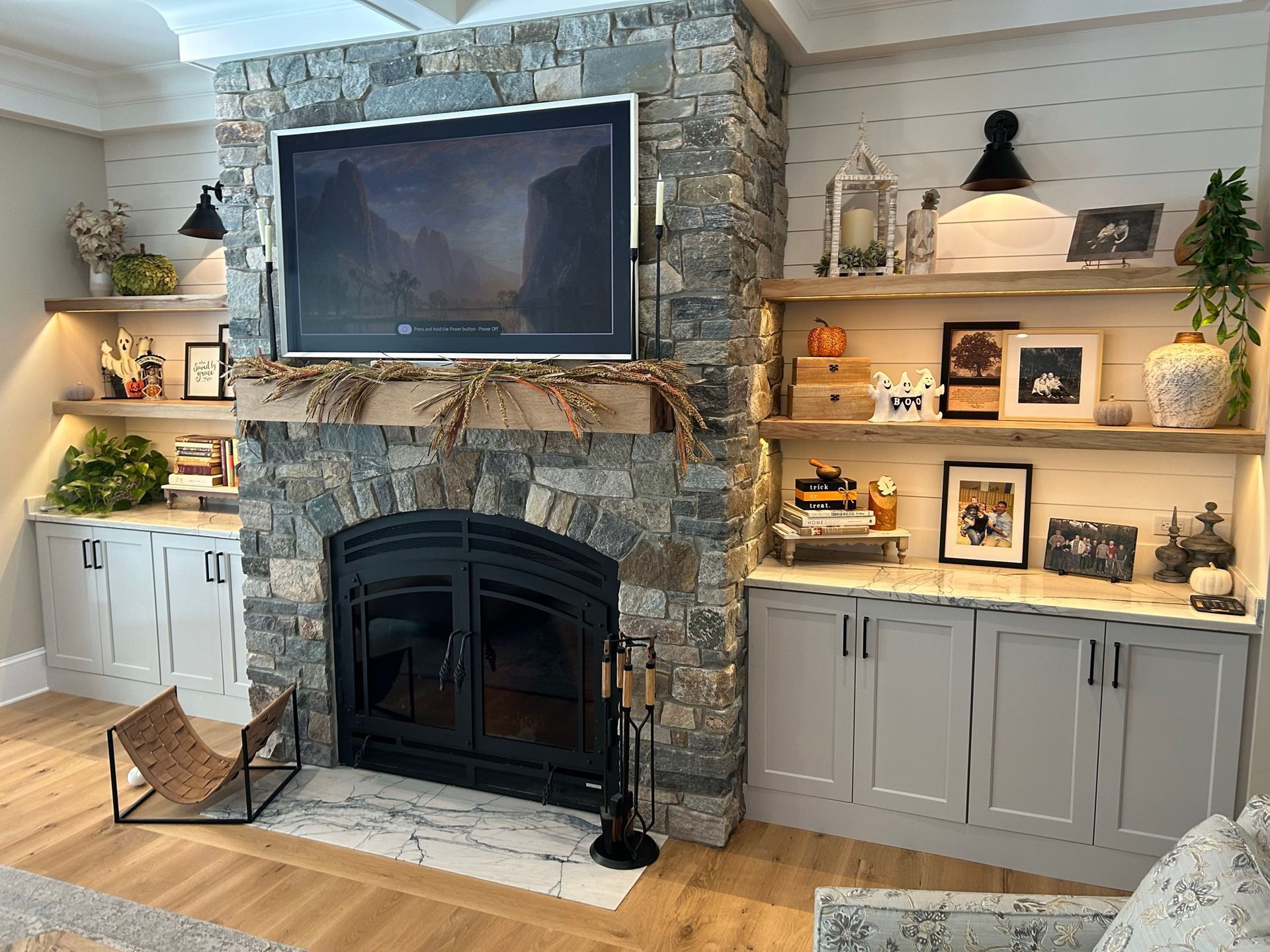 Living room with a stone fireplace, TV, built-in shelves, and white cabinets.