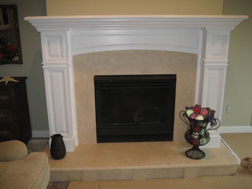 White fireplace with black insert, beige stone surround, and decorative vase.