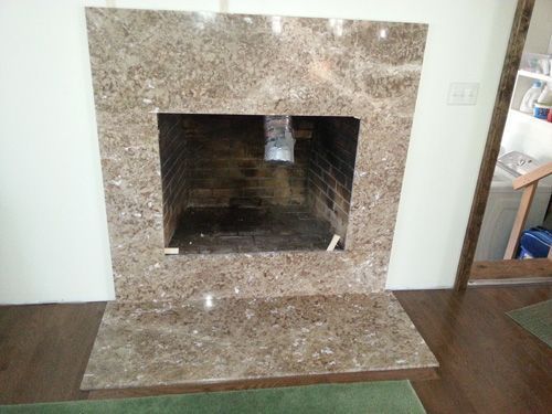 Fireplace with brown marble surround and hearth against a white wall.