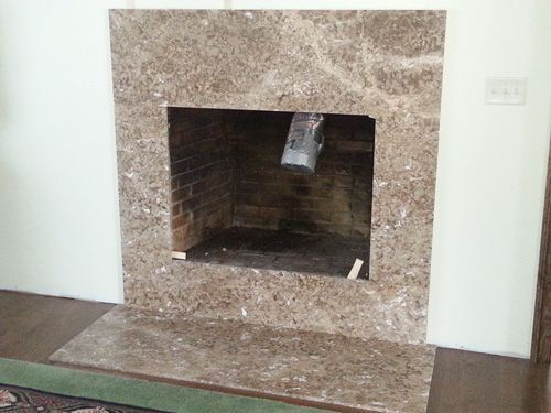 Fireplace with brown marble surround and hearth against a white wall.