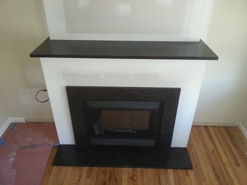 Fireplace with black granite hearth, surround, and mantle on a white frame, with hardwood floors.
