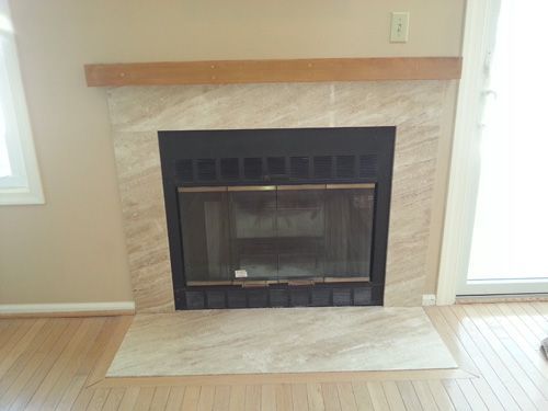Fireplace with tan marble surround and wooden mantel.