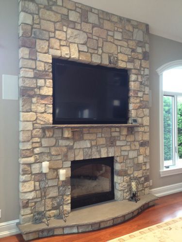 Stone fireplace with built-in TV. Beige stone, dark TV screen, candles, and a window.
