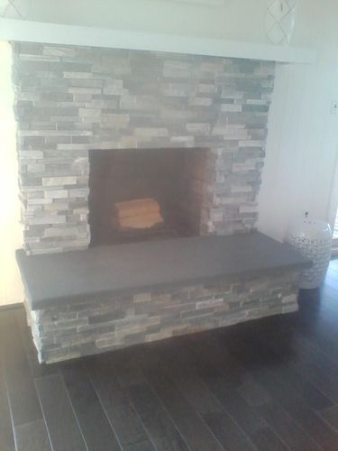 Stone fireplace with a gray hearth and dark wood flooring.
