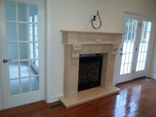 Fireplace with light-colored stone surround, flanked by glass doors, set in a room with hardwood floors.
