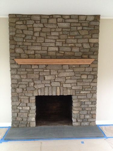 Stone fireplace with wood mantel and slate hearth against a light beige wall.