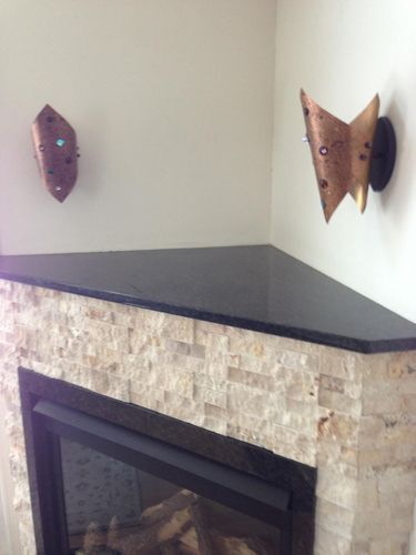 Corner fireplace with cream-colored stone facade and black granite top. Copper sconces adorn the wall.