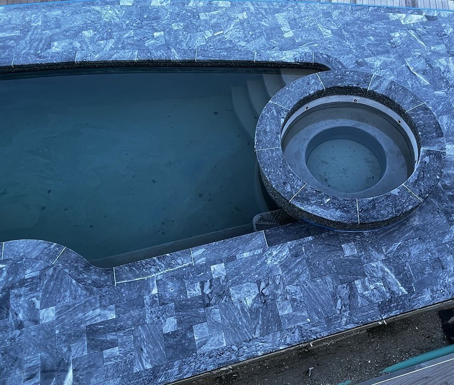 Pool and hot tub with dark stone tiling surround.