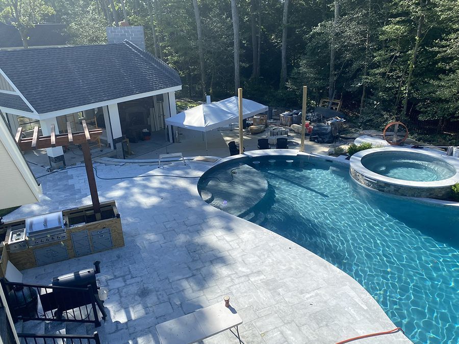Backyard with pool, spa, patio, and outdoor kitchen; surrounded by trees.