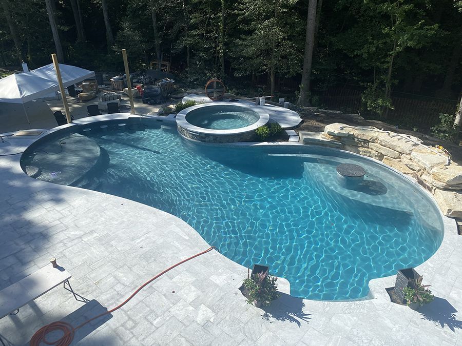 Outdoor swimming pool with attached hot tub, set in a natural, wooded environment.