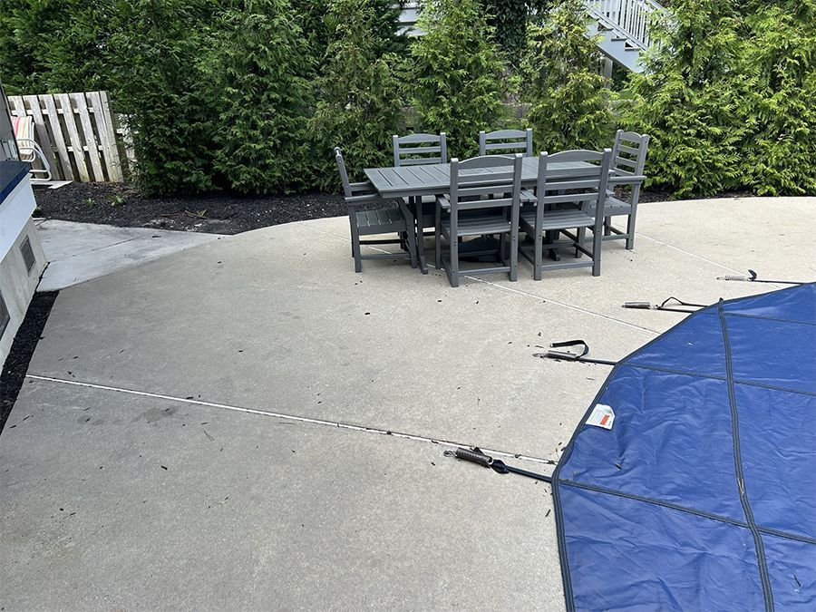 Patio with gray table and chairs. Blue pool cover in the foreground, trees in the background.