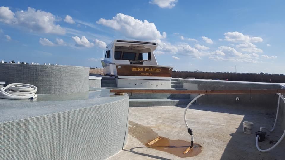A boat-shaped pool with a deck, against a cloudy blue sky.