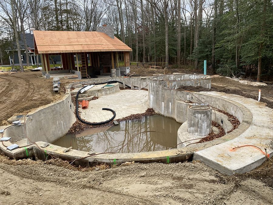 Pool construction site with concrete pool foundation, dirt, and new house in background.
