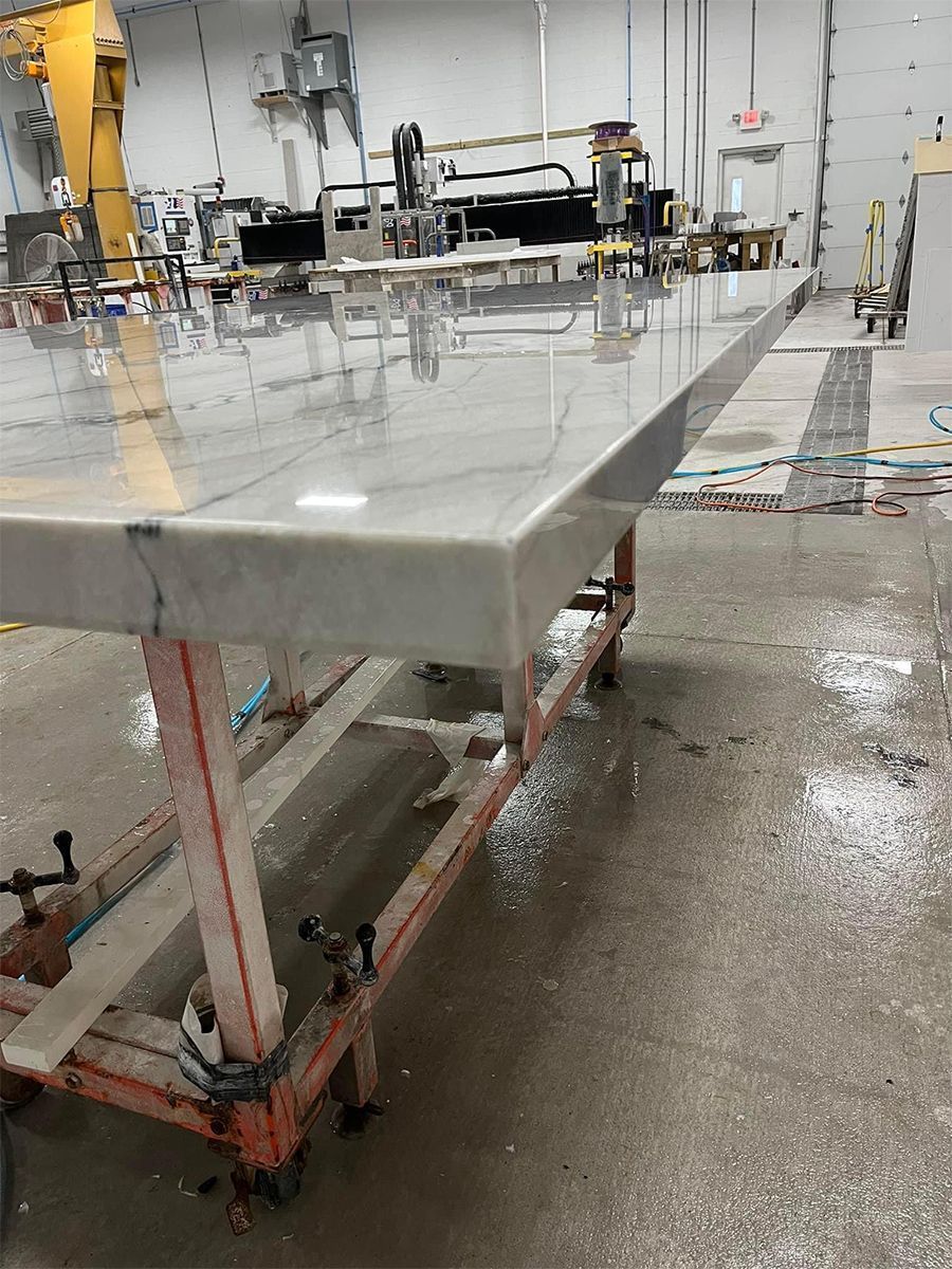 Large marble countertop on a red metal support in a workshop, with wet floors and machinery in the background.
