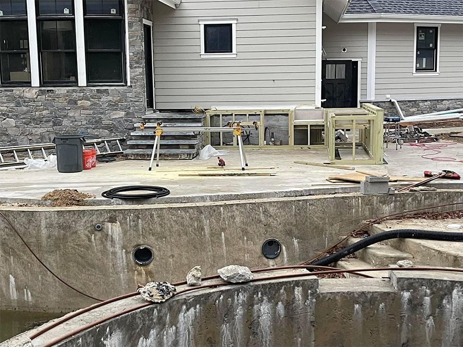 Construction site with partially built concrete pool and house. Equipment and debris visible.