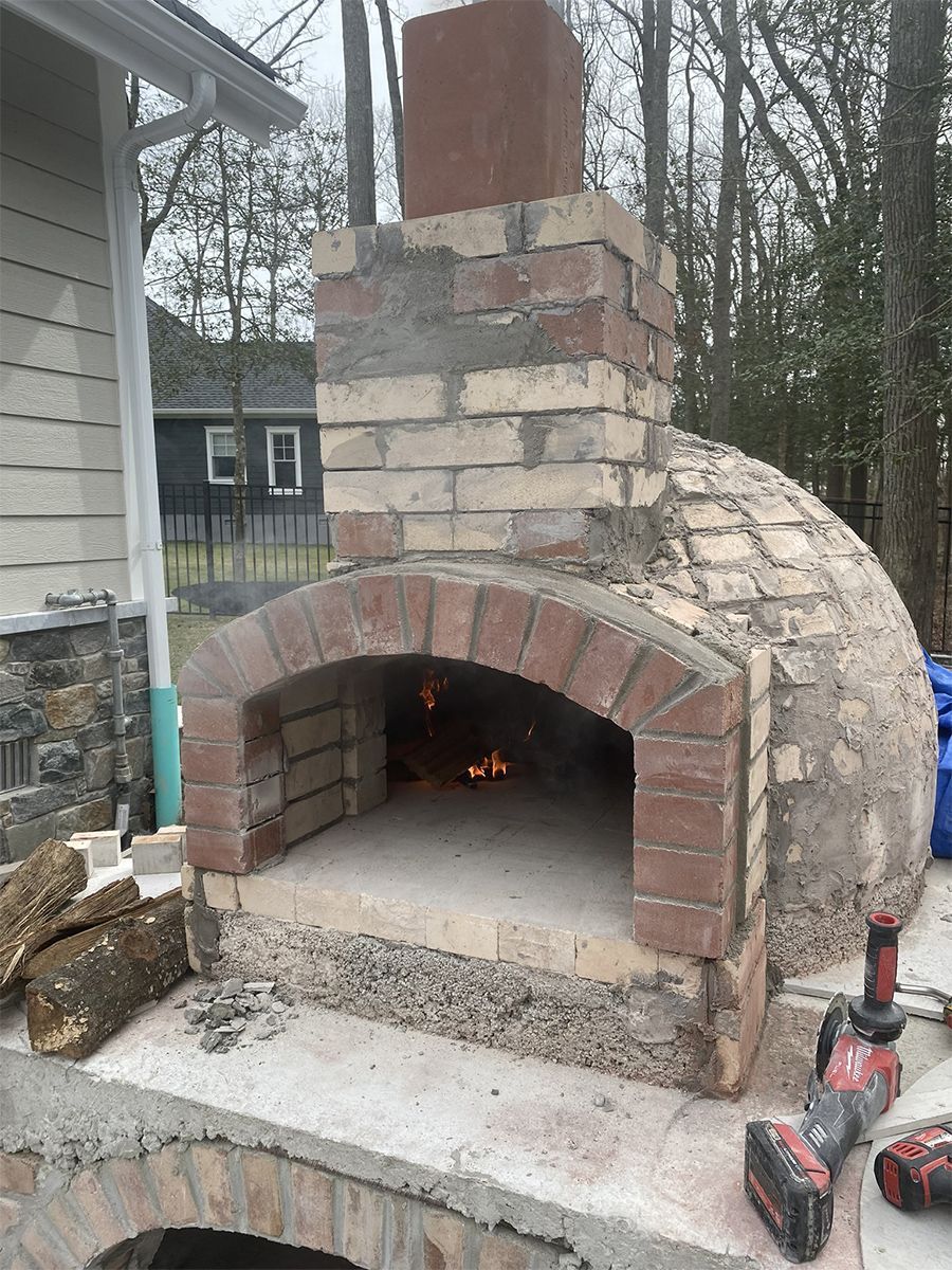 Brick outdoor pizza oven with fire burning inside.