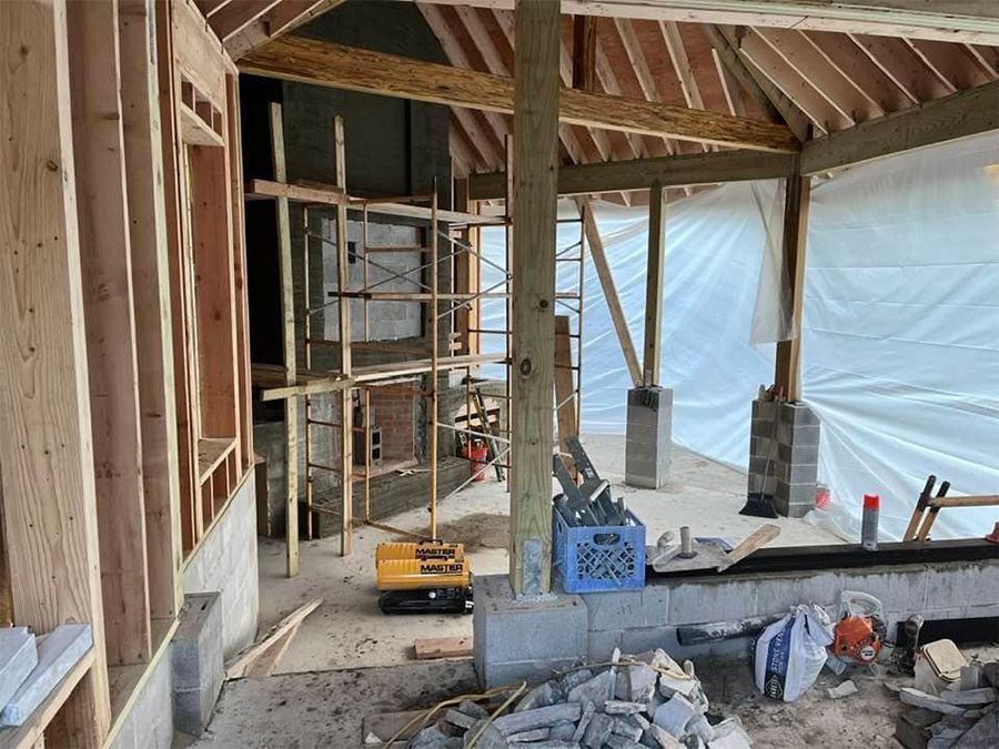 Construction site: Wooden framing, scaffolding, excavator, unfinished stone building, protective sheeting.