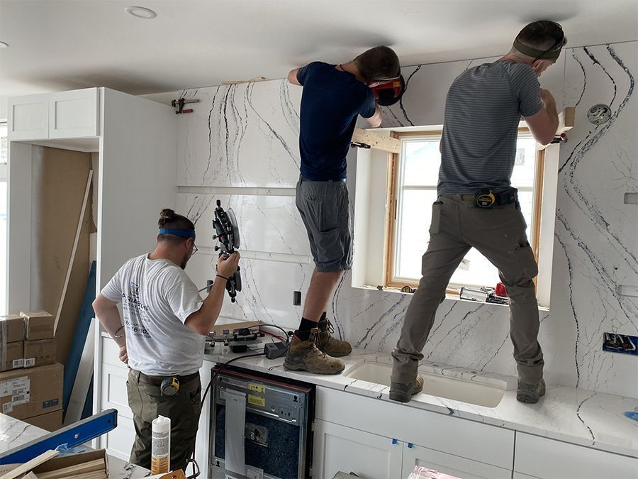 Three construction workers installing a countertop in a kitchen.