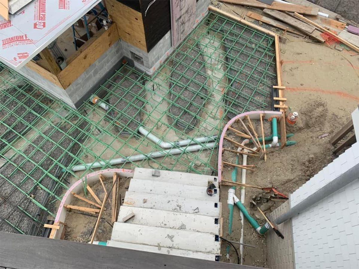 Construction site with rebar grid and plumbing for concrete steps and a landing.