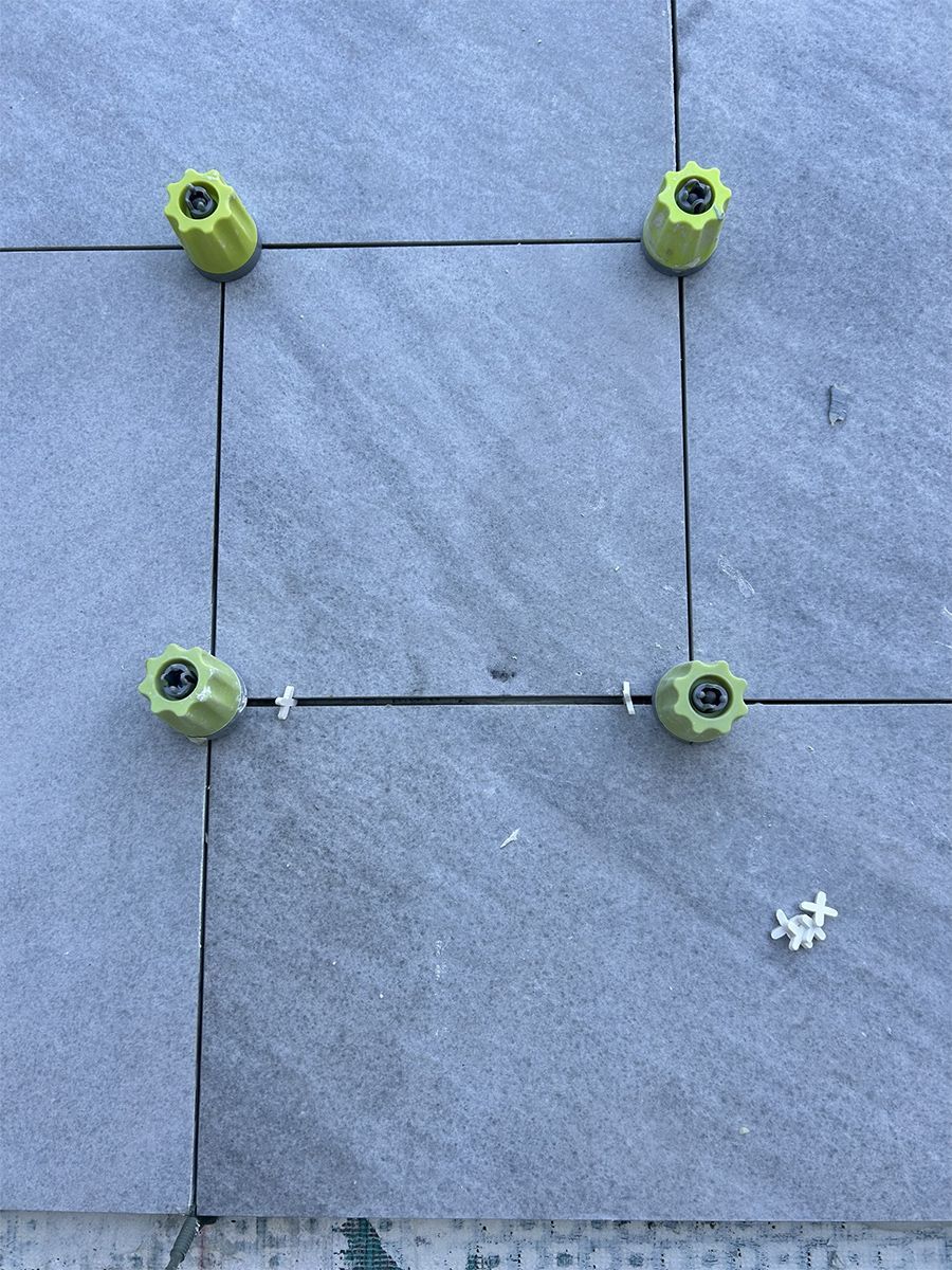 Four gray tiles with leveling system components: yellow caps and white spacers.