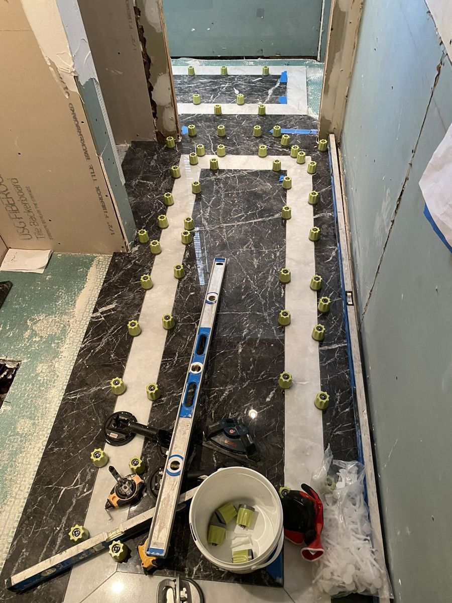 Bathroom floor tiling in progress: black and white tiles, leveling tools, spacers, bucket.
