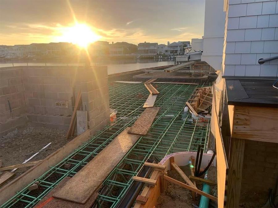 Construction site with rebar, wood, and concrete in front of water at sunset.