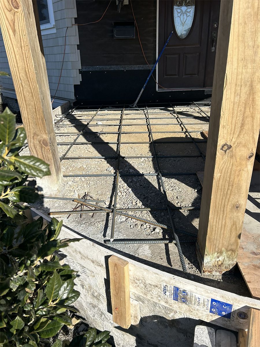 Concrete slab with exposed rebar, between wooden posts; front porch construction.