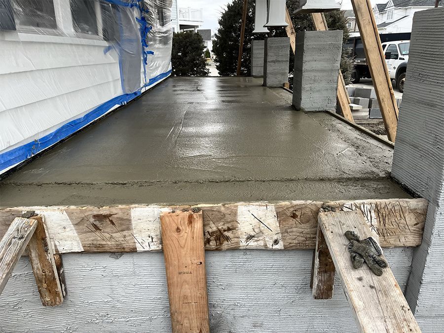 Freshly poured concrete patio with wooden framing and columns under construction.