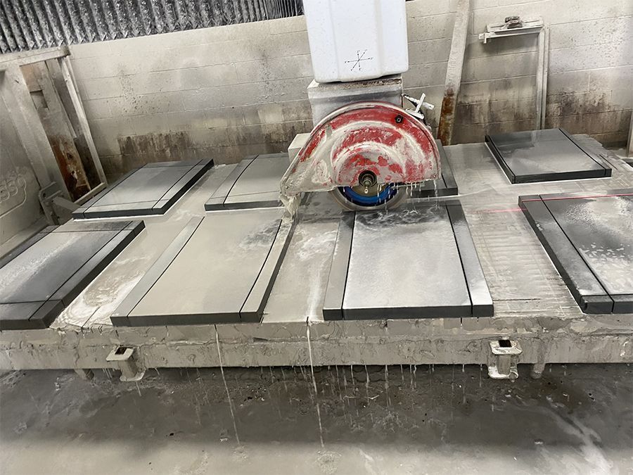 A large stone cutting machine sawing rectangular stone slabs with water spray in a factory setting.