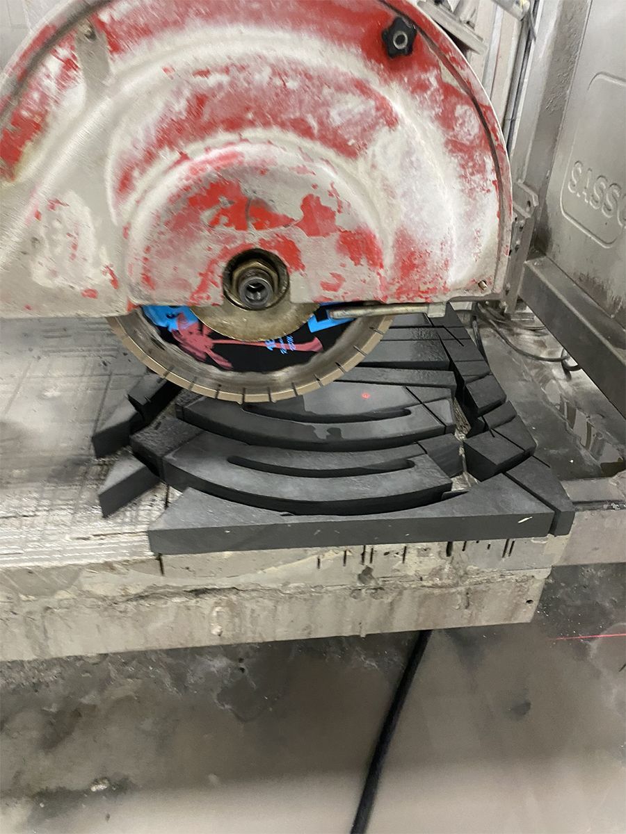 Tile saw with a red blade, cutting dark curved tile pieces.